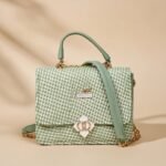 small green woven crossbody bag with a floral-shaped clasp.