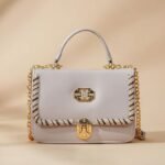 light-colored top-handle handbag with gold-tone hardware and chain details.